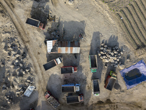 Aerial view of trucks clustered near a corrugated metal structure amidst the dusty terrain, casting long shadows, Klaten, Central Java, Indonesia.