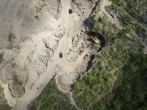 Aerial view of earthmoving machines scarring pale terrain, digging deep, shadowed pits, starkly contrasting with lush green, Klaten, Central Java, Indonesia.