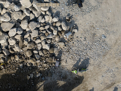 Aerial view of a rugged landscape where diligent workers move large, dark grey boulders across a dusty expanse of lighter gravel, Klaten, Central Java, Indonesia.