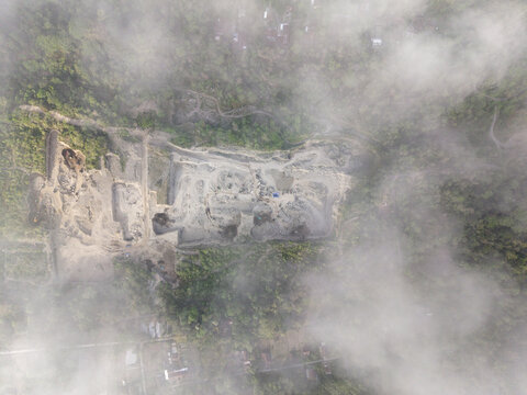 Aerial view of a construction site surrounded by lush greenery, partially obscured by clouds, creating a surreal blend of industry and nature, Klaten, Central Java, Indonesia.
