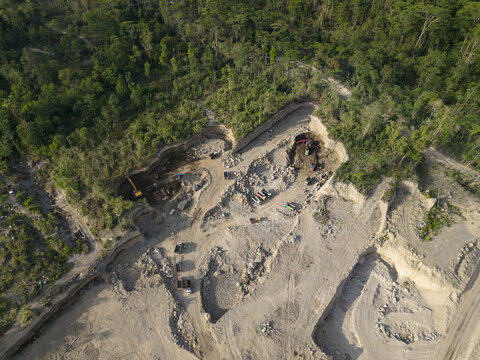 Aerial view of a stark excavation site carving into the vibrant green forest, revealing raw earth tones against the rich canopy, Klaten, Central Java, Indonesia.