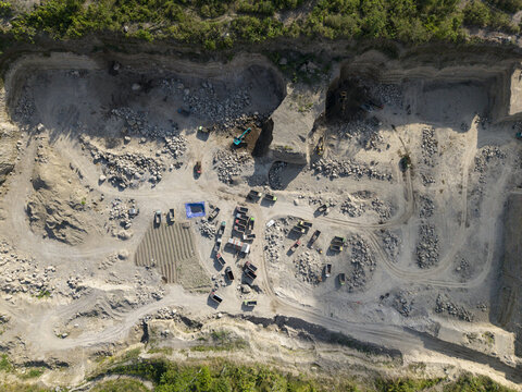 Aerial view of a quarry excavation site, with heavy machinery amidst the dusty terrain, contrasting sharply with the green vegetation, Klaten, Central Java, Indonesia.