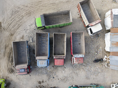 Aerial view of colorful dump trucks with open beds parked on a vast, dusty industrial lot, Klaten, Central Java, Indonesia.