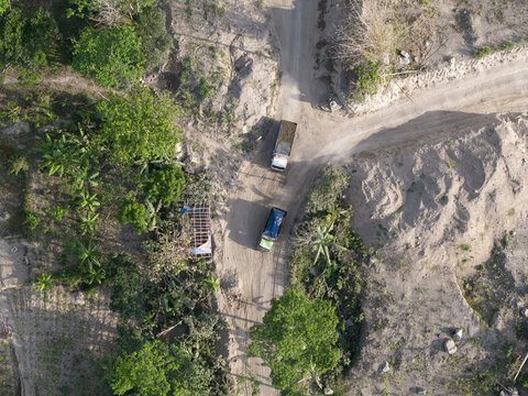 Aerial view of two trucks on a branching dirt road, a striking contrast of green foliage and pale, parched earth, Klaten, Central Java, Indonesia.