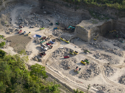 Aerial view of an active quarry, with heavy machinery on barren earth contrasting with vibrant green foliage, Klaten, Central Java, Indonesia.