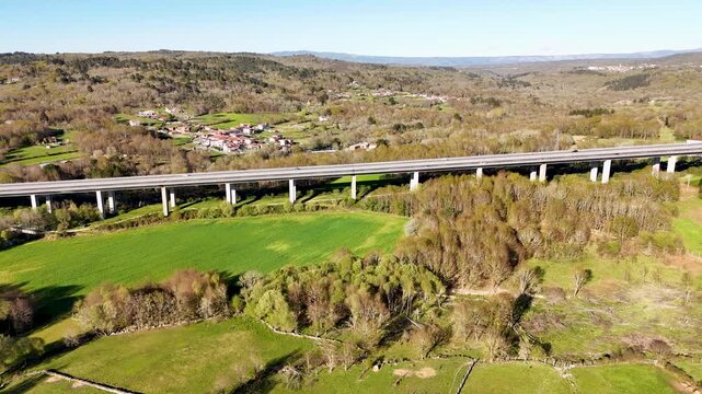 Aerial view of Viaducto Arnoia bridge spanning a verdant valley with rolling hills and a small village Allariz, Province of Ourense, Spain.