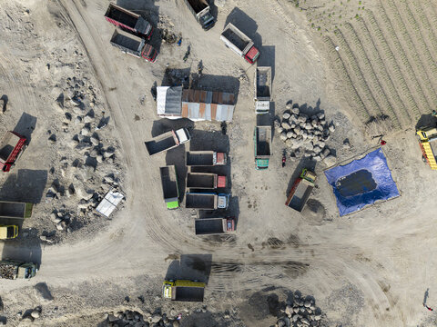 Aerial view of a dusty open-pit quarry, where numerous trucks and aggregate piles create stark patterns on the sun-baked earth, Klaten, Central Java, Indonesia.