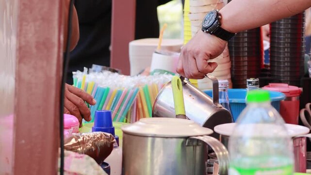 Vendor preparing traditional drinks at outdoor street market stall with colorful supplies.