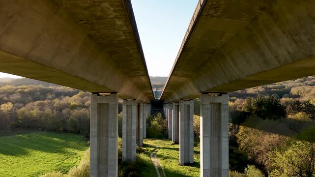 Aerial view of Viaducto Arnoia showing massive concrete pillars over a lush green valley during sunset in Allariz, Province of Ourense, Spain.