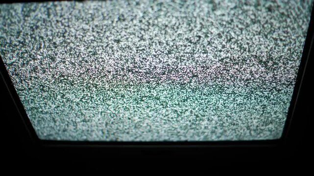 A close-up view of an old analog television screen filled with flickering static white noise. Concept of technical difficulties, signal loss, retro technology, and horror atmosphere.