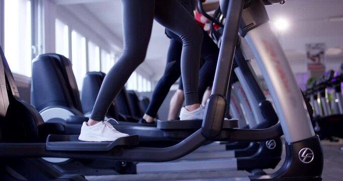 Close up of person legs in white sneakers exercising on an elliptical trainer in a fitness club