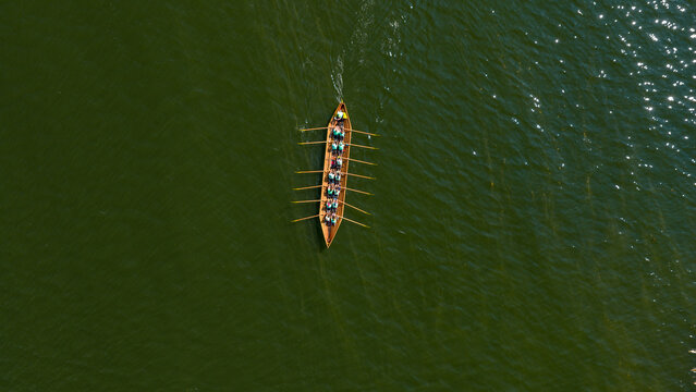 Aerial view of a sleek wooden rowing boat with a crew cutting through the shimmering emerald green waters with rhythmic strokes, Hiittinen, Southwest Finland, Finland.