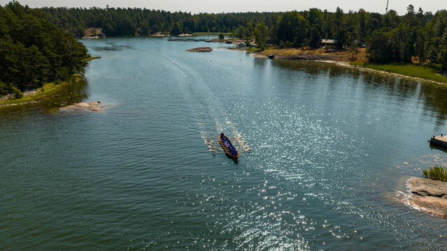 Aerial view of a lone kayak cuts through the shimmering, sun-drenched waters, flanked by verdant islands and rocky shores, Hiittinen, Southwest Finland, Finland.