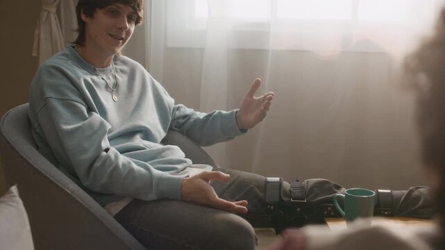 Ex young adult biker resting on chair and gesticulating while telling about results of moto accident