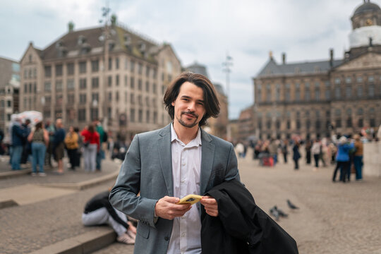 Young man using smartphone on dam square, amsterdam, traveling and exploring european city