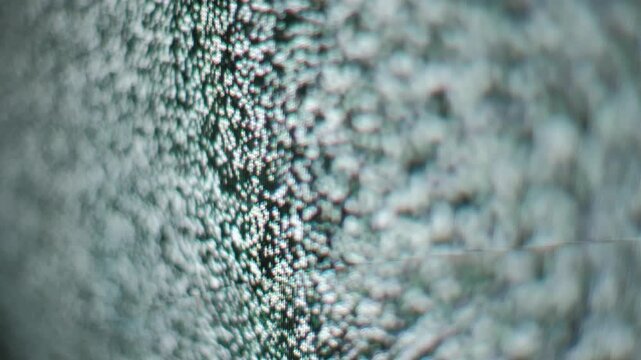 An out-of-focus view of flickering static noise on a TV screen creates a grainy texture. Concept of technical difficulties, retro technology, signal interference, and digital glitches.