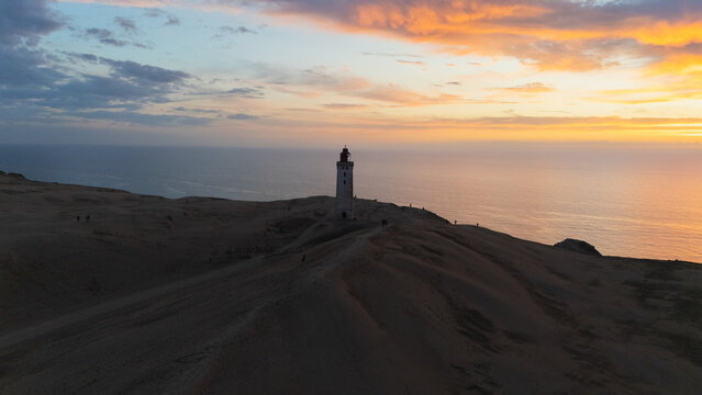 Aerial view of Rubjerg Knude Fyr lighthouse on dark, sculpted dunes, under a fiery sunset over the calm sea, Rubjerg Knude Fyr, North Denmark Region, Denmark.
