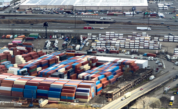 Aerial view of a vast logistics hub, where a vibrant tapestry of stacked shipping containers contrasts with the muted industrial landscape, Elizabeth, New Jersey, United States.