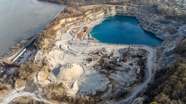 Aerial view of a sprawling quarry with a striking azure lake nestled amidst rugged rock walls and industrial machinery, Tomkins Cove, New York, United States.