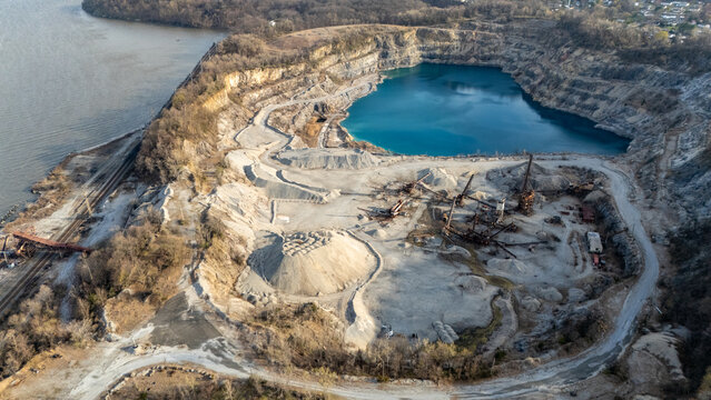 Aerial view of a quarry's stark, layered terraces meet a lake's serene blue, creating a striking contrast of industry and nature, Tomkins Cove, New York, United States.