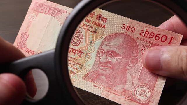 Examination of 20 Indian rupees (INR) cash money with magnfication glass, loupe. Concept of authenticity check, fight against counterfeiting of banknotes, anti fraud measures in India. Close up view.