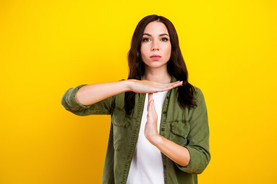Young woman making a time-out hand gesture against a bright yellow background, conveying pause, refusal and assertive boundary setting