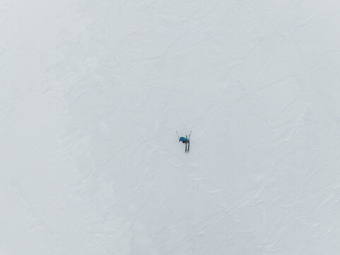 Aerial view of a lone skier in blue carving pristine tracks across a vast, pure white snowfield, Piano Provenzana, Sicilia, Italy.