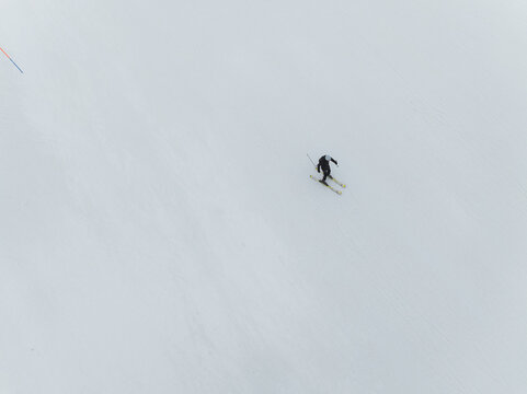 Aerial view of a lone skier on a pristine white slope, a dark figure contrasting with the vast snowy expanse, Piano Provenzana, Sicilia, Italy.
