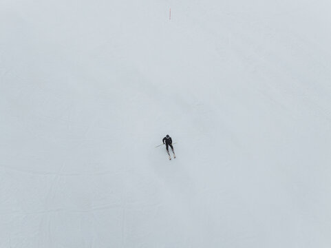 Aerial view of a lone skier descending a pristine white slope, their dark gear a stark contrast against the pure snow, Piano Provenzana, Sicilia, Italy.