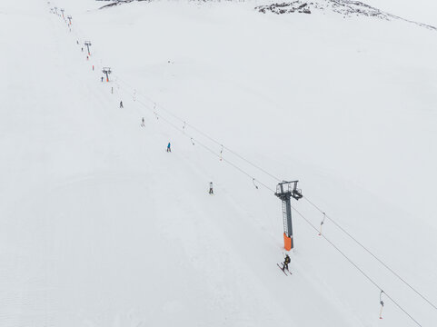 Aerial view of skiers on vast white slopes with prominent dark ski lift towers, Piano Provenzana, Etna Nord, Linguaglossa, Sicilia, Italy.