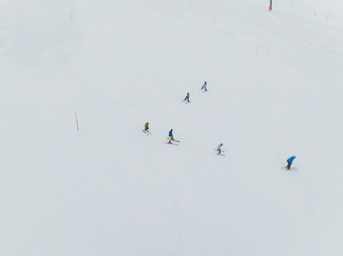 Aerial view of colorful skiers descending a vast, pristine white snowfield, leaving delicate tracks across the smooth expanse, Piano Provenzana, Sicilia, Italy.