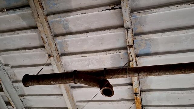 Interior view of an abandoned industrial building ceiling of a tobacco factory in Yelets. Close up of rusty metal pipes and peeling paint on concrete structures