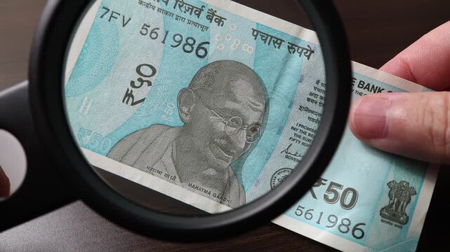 Examination of 50 Indian rupees (INR) cash money with magnfication glass, loupe. Concept of authenticity check, fight against counterfeiting of banknotes, anti fraud measures in India. Close up view.