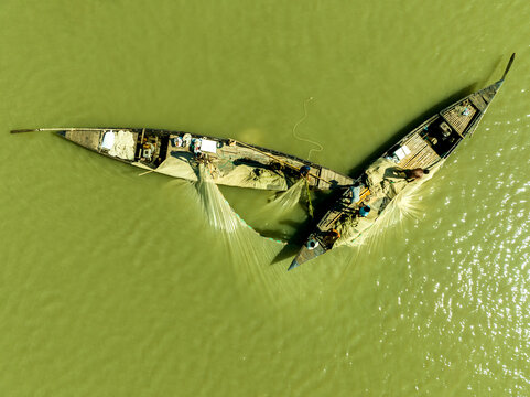 Aerial view of two dark wooden boats with fishing nets dramatically spread across calm, murky green waters, Bogura, Rajshahi Division, Bangladesh.