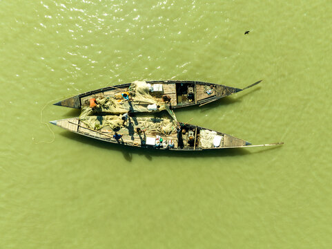 Aerial view of two traditional fishing boats, laden with nets, resting on the calm, murky green waters, Bogura, Rajshahi Division, Bangladesh.