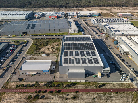 Aerial view of a sprawling modern industrial complex featuring sleek grey warehouses adorned with dark solar panels, interconnected by asphalt roads, Vagos, Aveiro, Portugal.