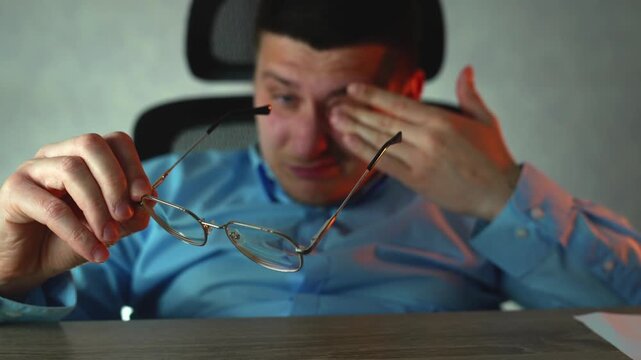 Young professional suffering from tired eyes, taking break while working late. Eye strain and stress from prolonged computer use in office