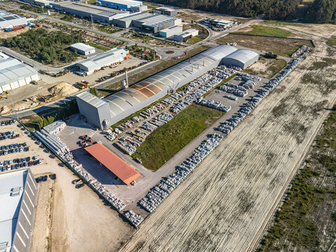 Aerial view of a large industrial complex, showcasing a curved-roof factory, vast rows of precast concrete, and stark sandy grounds, Vagos, Aveiro, Portugal.