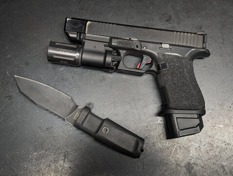 Baltic States, April 24, 2026: Tactical gear composition featuring an Extrema Ratio TASK C fixed blade knife and a custom Glock 19 Gen 5 pistol with weapon light and compensator. 