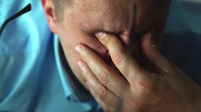 Young professional suffering from tired eyes, taking break while working late. Eye strain and stress from prolonged computer use in office
