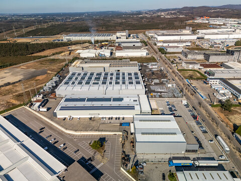 Aerial view of sprawling industrial complexes with gleaming solar panels under a vibrant blue sky, contrasting with undeveloped land, Albergaria-a-Velha, Aveiro District, Portugal.