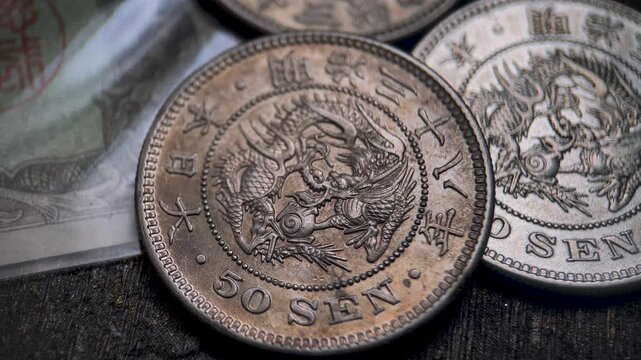 Close up video showing a collection of Japanese Meiji era 50 sen silver coins arranged together, highlighting intricate dragon obverse designs, Japanese inscriptions, and aged metallic surfaces.