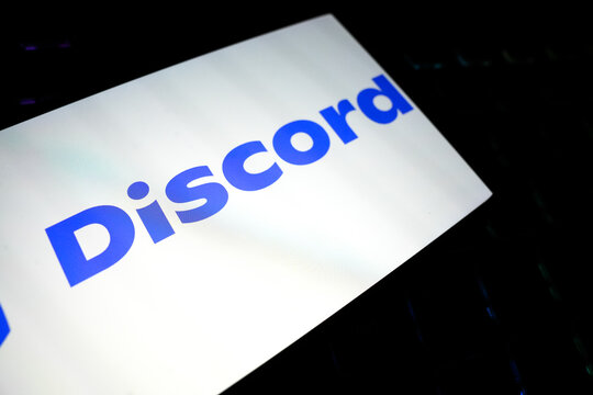 Discord Logo and Wordmark on a Bright White Smartphone Screen Tilted Over a Dark Keyboard, Representing Social Communication, Online Communities, Instant Messaging, and Digital Gaming Culture.