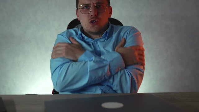 Cold office scene with businessman experiencing discomfort due to low temperature. He tries to stay warm by rubbing hands and self-hugging in poorly heated corporate environment.
