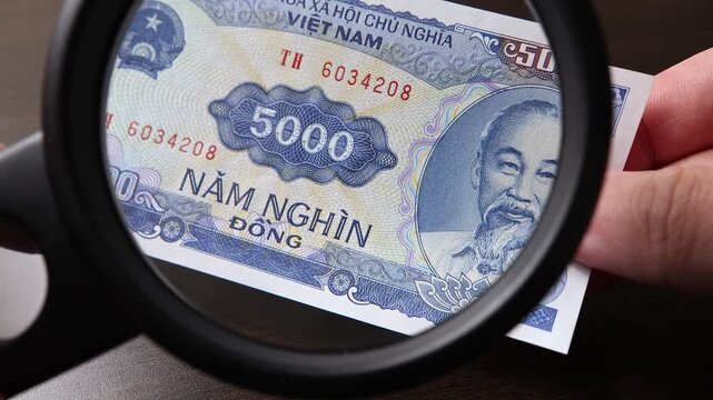 Examination of 5000 Vietnamese dong (VND) cash money with magnfication glass, loupe. Concept of authenticity check, fight against counterfeiting of banknotes, anti fraud measures in Vietnam.