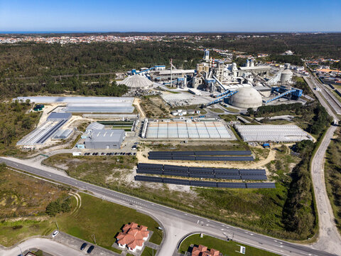 Aerial view of the industrial zone sprawling under a clear blue sky, juxtaposing the modern structures with the surrounding green landscape, Pataias, Leiria, Portugal.