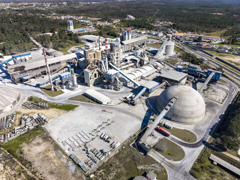 Aerial view of a sprawling industrial complex with dome structures and concrete elements contrasting against the lush green trees, Pataias, Leiria, Portugal.