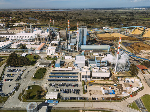 Aerial view of a sprawling industrial complex, its towering red and white smokestacks punctuating the horizon as steam billows into the crisp sky, Cacia, Aveiro District, Portugal.