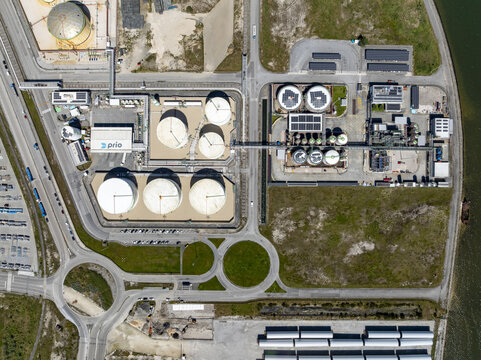 Aerial view of industrial tanks gleaming under the sun, amidst roads and structures, creating a stark contrast with the surrounding greenery, Sines, Portugal.