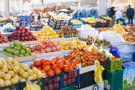 Colorful fresh produce stand at traditional oriental bazaar. Heaps of ripe oranges, tangerines, lemons, apples, pears, fuzzy kiwis and pomegranates in sunny morning. Samarkand Siab market, Uzbekistan.